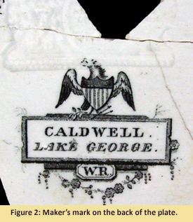 Back side of plate showing the makers mark shows a printed mark of an eagle and two boxes as well as a partial impressed mark of a lion. One of the boxes contains the printed words “Caldwell, Lake George” while the other box contains “W.R.”